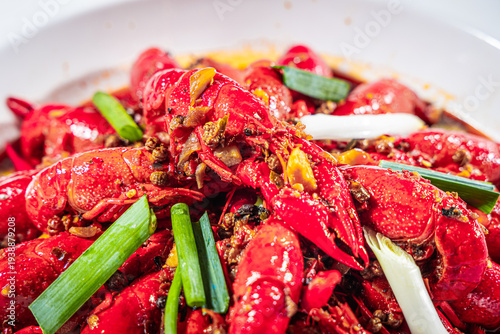 Close up of crayfish cooked in spicy sauce with chili garlic and scallion. The intense red color and glossy texture emphasize bold Chinese flavors suitable for seafood and spicy cuisine promotion.