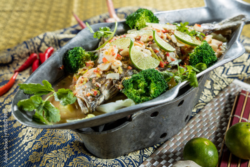 Fish pieces steamed in light broth with lime chili and vegetables served in a metal pot. The dish reflects Southeast Asian flavors and suits seafood and soup menu concepts.
