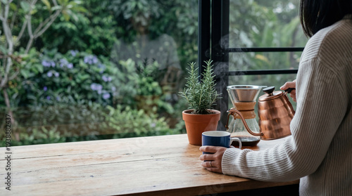 Woman preparing a fresh pour-over coffee with a stylish copper kettle by a lush green garden window.