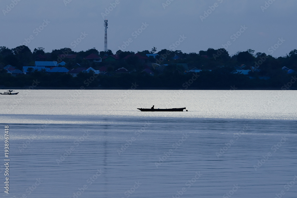 Obraz premium close up silhouette of a fisherman in a boat fishing in the sea. evening atmosphere with golden color. beautiful view suitable for wallpaper or background
