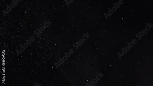 Deep black image with specks of light, resembling stars or dust particles