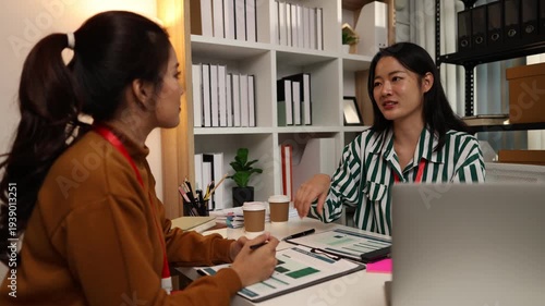 Two businesswomen discussing startup ideas and reviewing documents during a meeting in modern office, representing teamwork, business planning and collaboration in a startup company.