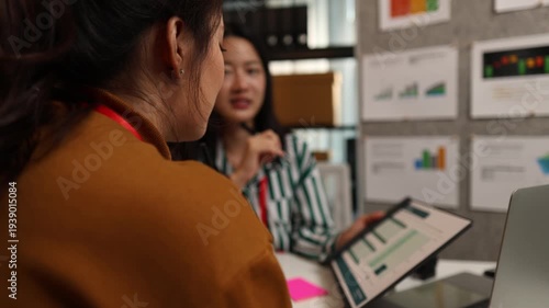 Two businesswomen discussing startup ideas and reviewing documents during a meeting in modern office, representing teamwork, business planning and collaboration in a startup company.