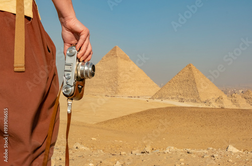 Person holding camera near the pyramids of Giza at midday in a desert landscape in Egypt while exploring historical sites