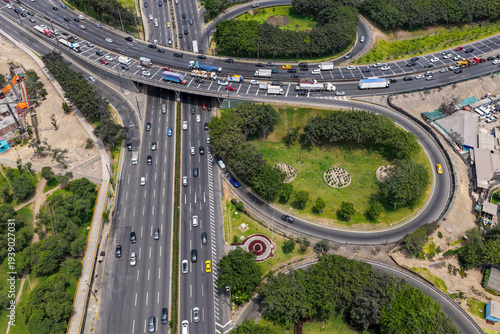 Aerial view of a highway in a city with a road interchange next to many gardens.