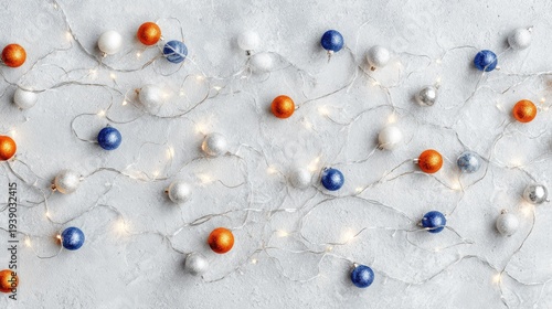 Festive holiday ornaments and glowing string lights are scattered across a light textured surface viewed from above