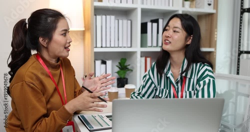 Two businesswomen discussing startup ideas and reviewing documents during a meeting in modern office, representing teamwork, business planning and collaboration in a startup company.
