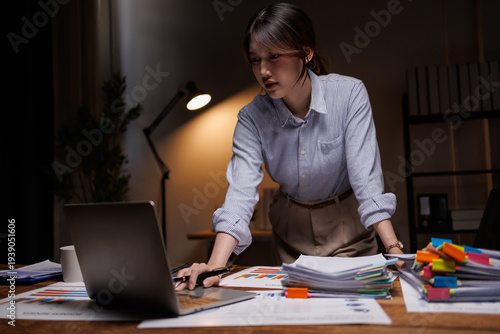 Bilde på lerret Focused Asian businesswoman standing at desk and using laptop while working late