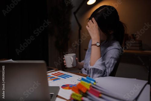 Thoughtful Asian businesswoman working late at night in dark office with laptop and paperwork