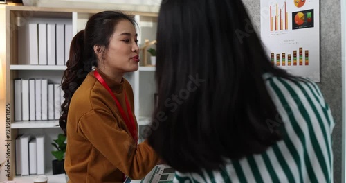Two businesswomen discussing startup ideas and reviewing documents during a meeting in modern office, representing teamwork, business planning and collaboration in a startup company.