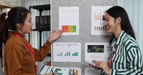 Two businesswomen discussing startup ideas and reviewing documents during a meeting in modern office, representing teamwork, business planning and collaboration in a startup company.