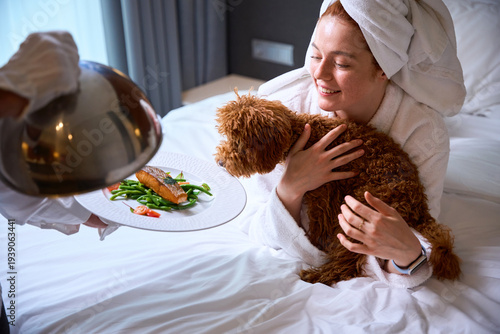 Tableau sur toile Young Caucasian woman cuddling dog in hotel bedroom during day