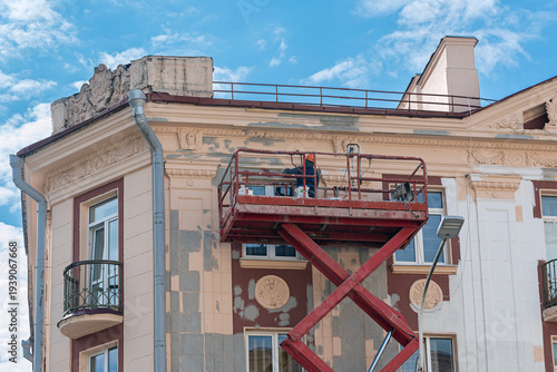 Construction worker in lift bucket of crane restore and repair historic facade of building