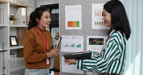 Two businesswomen discussing startup ideas and reviewing documents during a meeting in modern office, representing teamwork, business planning and collaboration in a startup company.