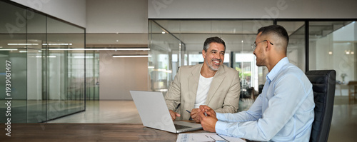 Happy professional business team people of two smiling latin executive business men having conversation on digital financial investment technology management using laptop computer working in office.