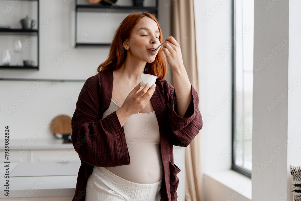 Fototapeta premium Pregnant woman enjoying healthy yogurt snack in kitchen, focusing on nutrition
