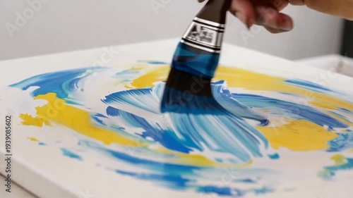 Person painting blue and yellow swirls on white canvas with brush