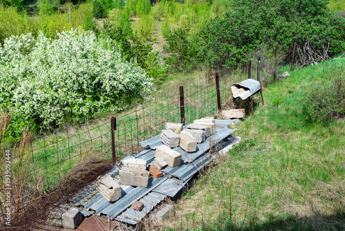 A ramshackle wire fence and remnants of construction materials against the backdrop of a rural landscape.
