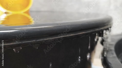 Water droplets falling from the edge of a large container with a bright orange dipper reflected in the water above.