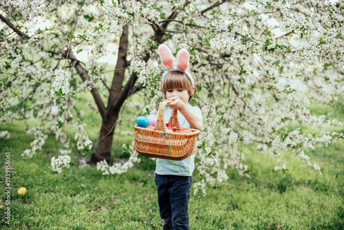 Easter egg hunt. child Wearing Bunny Ears Running To Pick Up Egg In Garden. Easter tradition. Baby with basket full of colorful eggs.