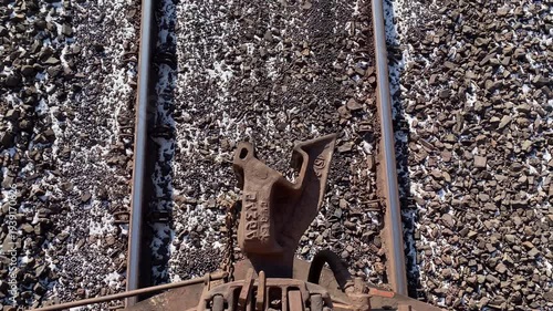 POV view from moving train over railway tracks with visible automatic coupler. Railway transport infrastructure and motion of train on metal rails.