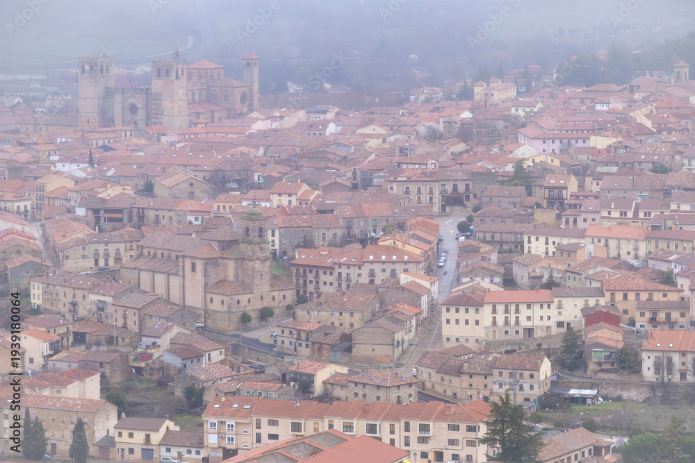 Obraz premium drone viewview of the historic town of Siguenza in Spain covered in thick winter fog featuring the medieval cathedral and traditional tiled roofs under a misty grey sky
