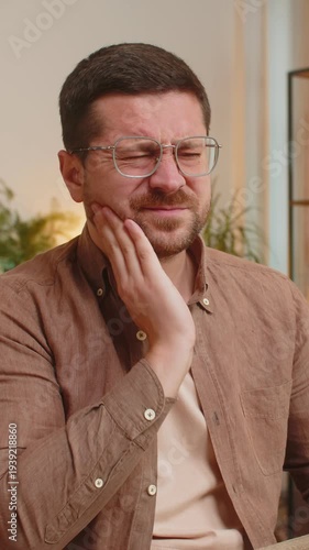 Caucasian young businessman freelancer sitting at home office table feeling toothache touching mouth with hand, painful expression because of dental illness, gum disease, dental disease concepts.