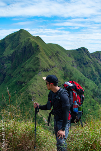 Male hiker with backpack and trekking poles looking at mountain