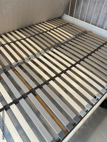 Slatted bed base with wooden planks inside bedroom frame. Close-up view of orthopedic mattress support system. Furniture assembly concept for home interior renovation and design.