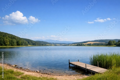 Wallpaper Mural Serene lake water reflecting a clear blue sky, with a simple wooden pier inviting quiet moments amidst green hills and distant mountain views offering peaceful natural scenery Torontodigital.ca