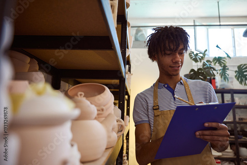 Young African American man writing in pottery workshop