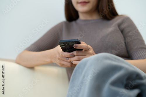 Photography Young asian woman sitting on a sofa at home using smartphone surfing the net for social media network, modern people lifestyle