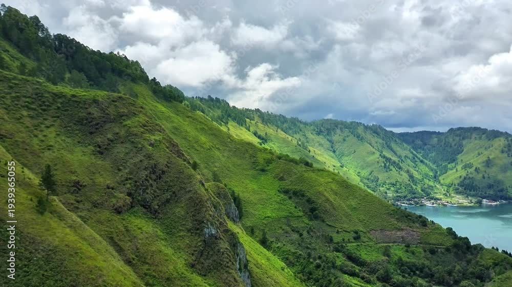 custom made wallpaper toronto digital4K aerial drone footage flying near a green hillside along Lake Toba, showing lush vegetation, pine trees, and rolling hills with a glimpse of calm lake water under cloudy daylight