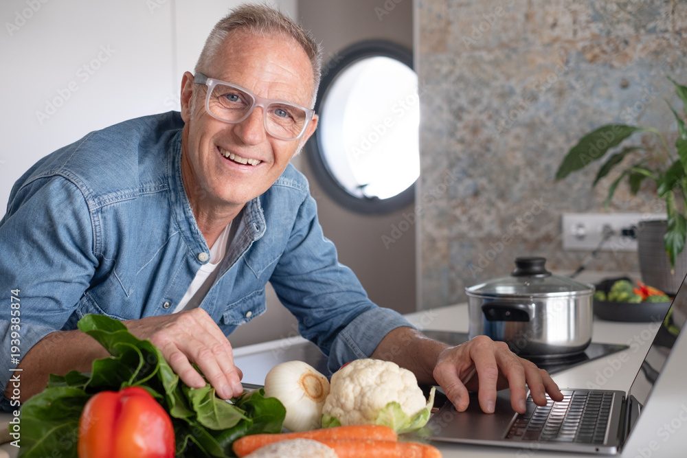 © luciano - Smiling mature man searching for new recipes on his laptop while cooking healthy food at home in a modern kitchen, preparing vegetables. Concept of nutrition, active lifestyle, and healthy eating © luciano - Smiling mature man searching for new recipes on his laptop while cooking healthy food at home in a modern kitchen, preparing vegetables. Concept of nutrition, active lifestyle, and healthy eating