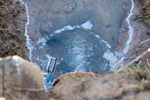 Photos Glass bottle as waste in polluted water, problem of littering natural environment and groundwater, close-up of contaminated drainage ditch with foam and trash