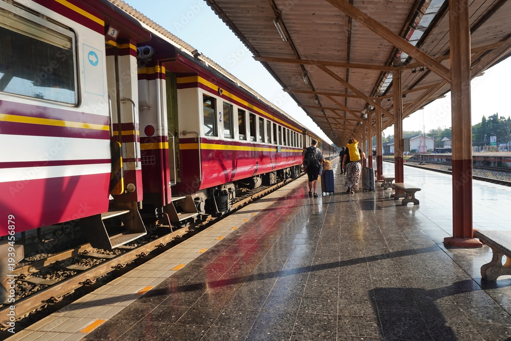 Obraz premium The daytime atmosphere at the train station, with a train parked on the platform as passengers and travelers carrying luggage walk along the station.
