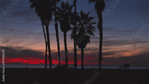 Lifeguard tower and palm silhouettes against red sunset sky