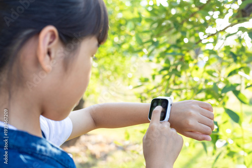 Tableau sur toile A young Chinese girl using a children's smartwatch in a park