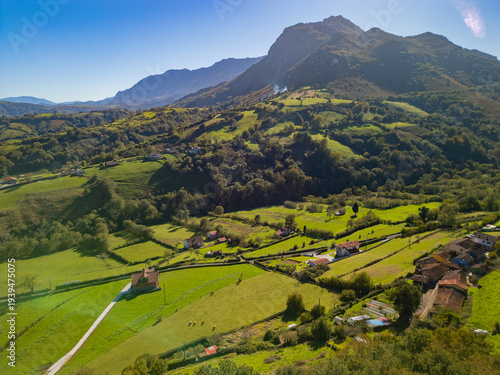 Epic green mountain valley panorama. 
Cinematic aerial drone view 
of rural farmland and 
Picos de Europa mountains 
in Asturias, Spain.
