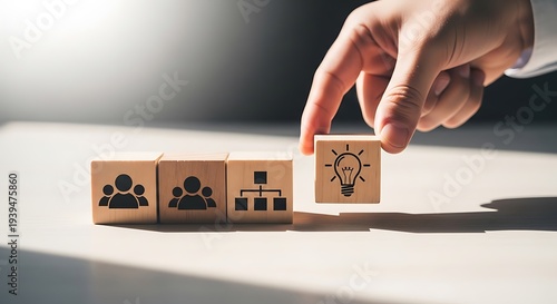 Person's hand placing wooden block with lightbulb icon next to blocks with people and organization charts symbolizing idea generation and teamwork.