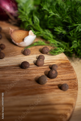 Foto Whole allspice seeds on a wooden kitchen board in sunlight