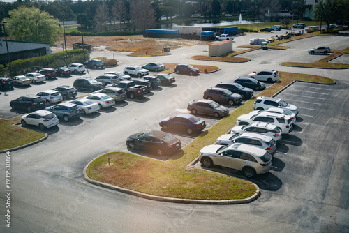 Photos Wide overhead scene of a sunlit parking lot with rows of vehicles, curved median