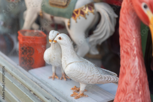Ceramic white pigeon figurines displayed in a shop window with a price tag.