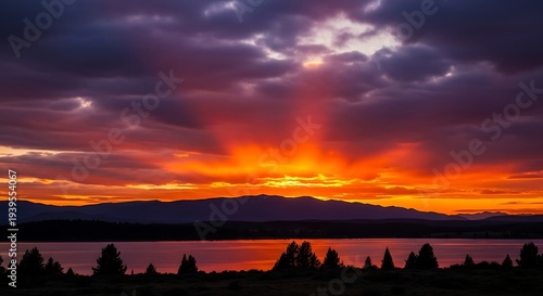 Vibrant sunset over serene lake with silhouetted trees and mountains