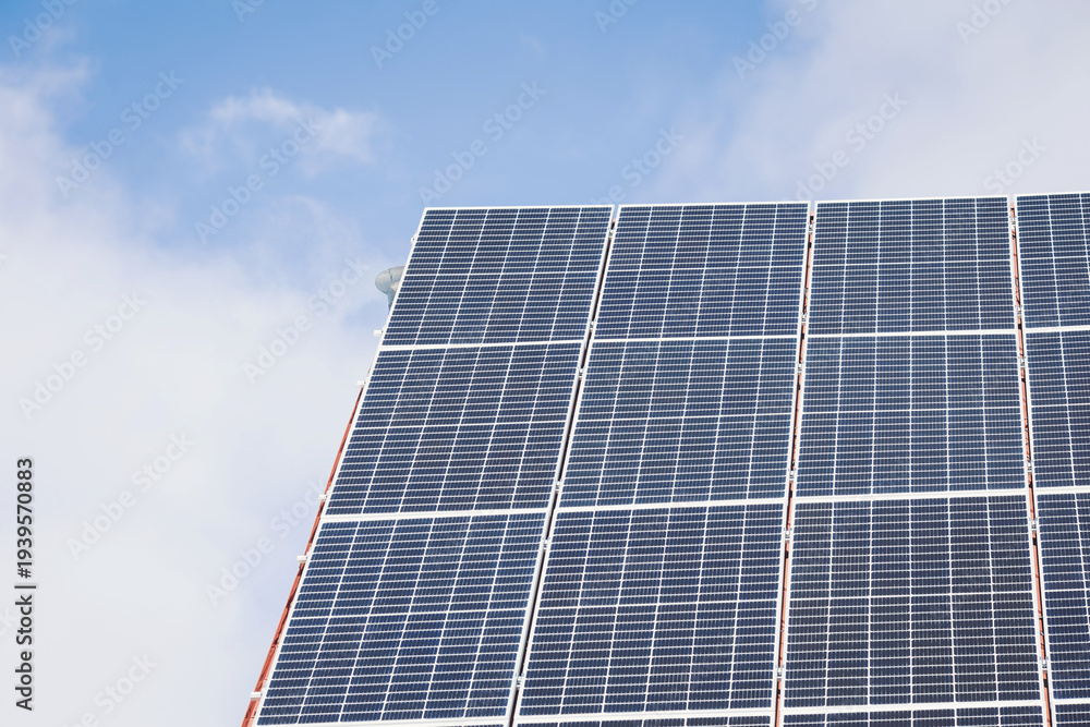 Naklejka premium Solar panels stand tall against a backdrop of soft clouds and a vibrant blue sky. This scene captures the essence of renewable energy shining brightly in the afternoon sun