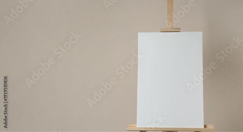 Blank white canvas on wooden easel against beige background