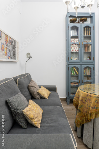 Cozy living room interior with a gray sofa, decorative pillows, vintage style display cabinet, and round table