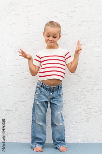 little girl standing, making funny face as if she doesn't
know in front of white wall
