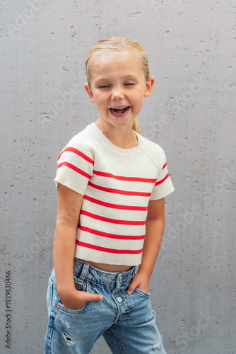young girl laughing out loud with striped shirt and jeans in front of grey background