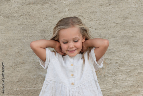 sweet happy smiling little girl looking down, arms behind her neck, natural look